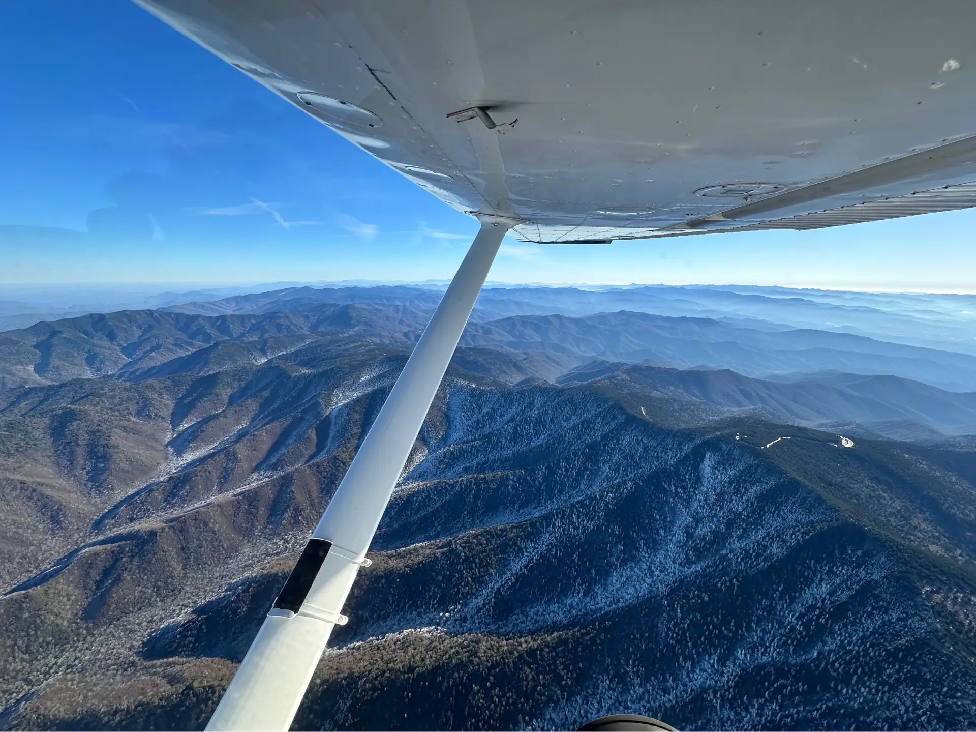 View of mountains and plane wing from the cockpit window of a flying airplane