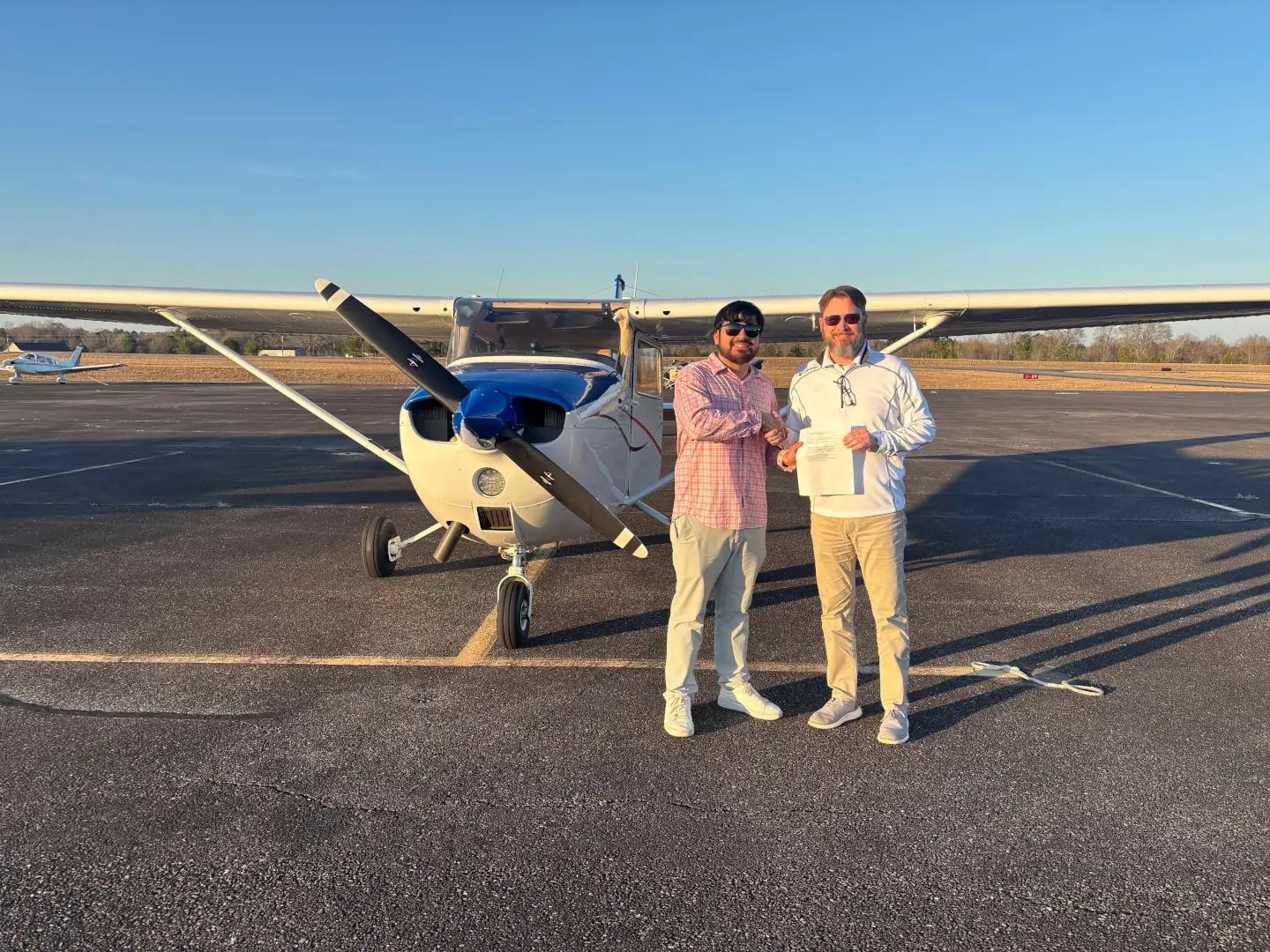Speedway student celebrating a training milestone beside another person and a Cessna in golden-hour light